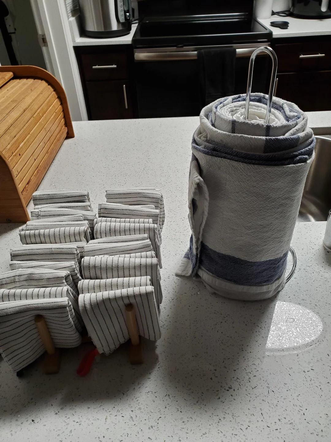 Neatly folded striped towels are organized on a kitchen counter next to a stack of rolled towels on a stand