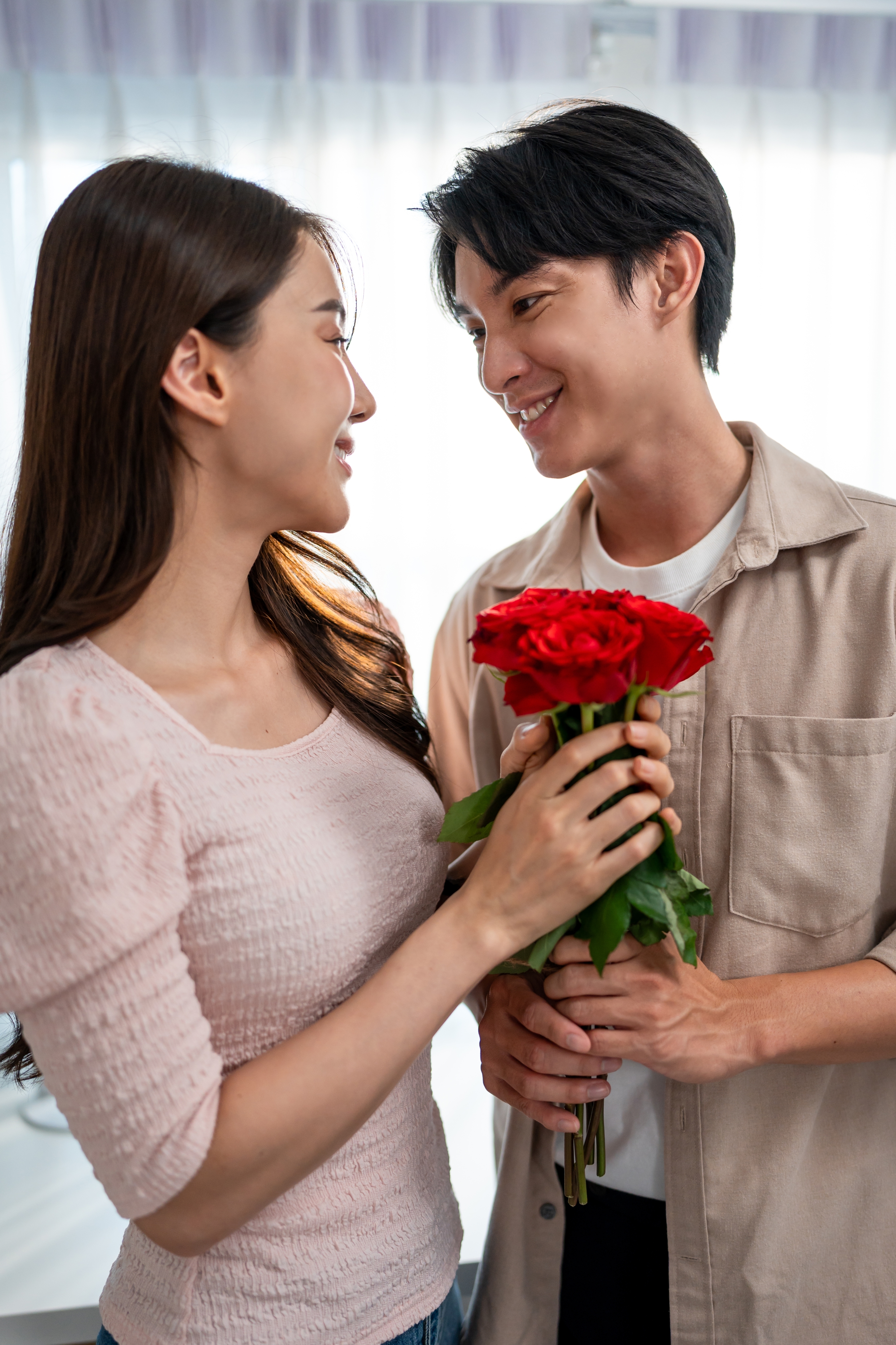 A couple smiling at each other; the man holds a bouquet of red roses, suggesting a romantic gesture