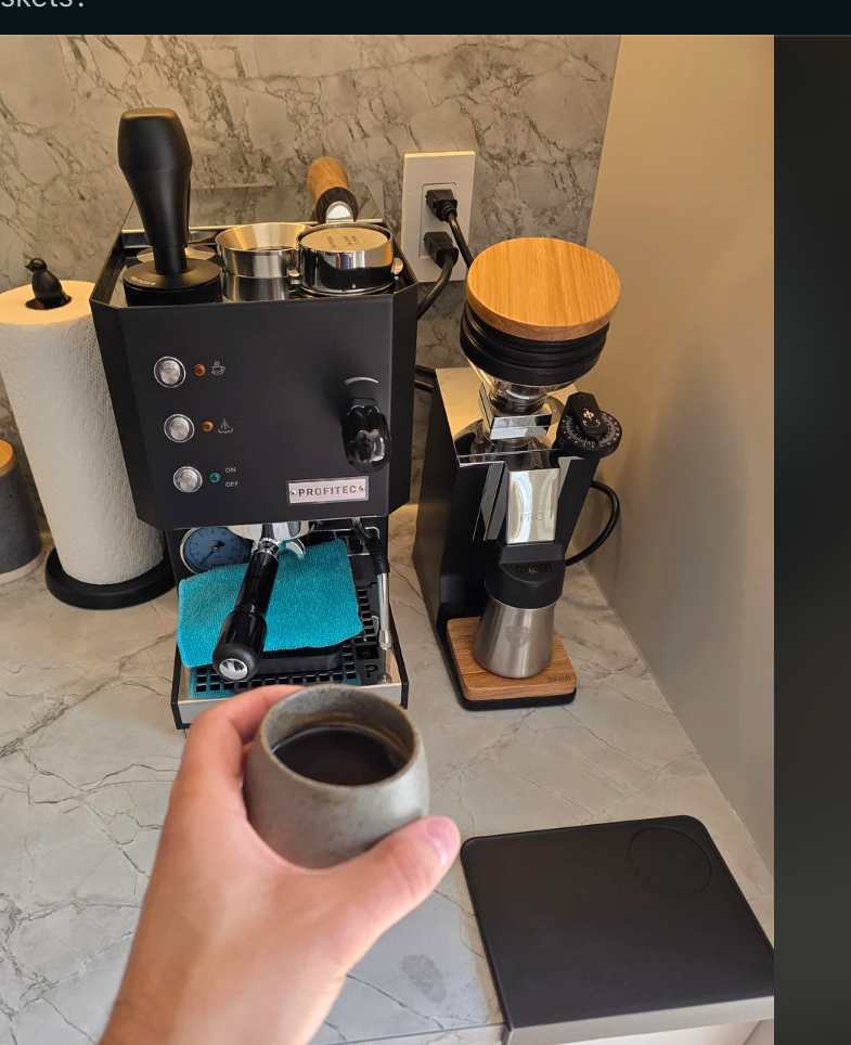 Person holding a cup of coffee next to a compact espresso machine setup on a kitchen counter