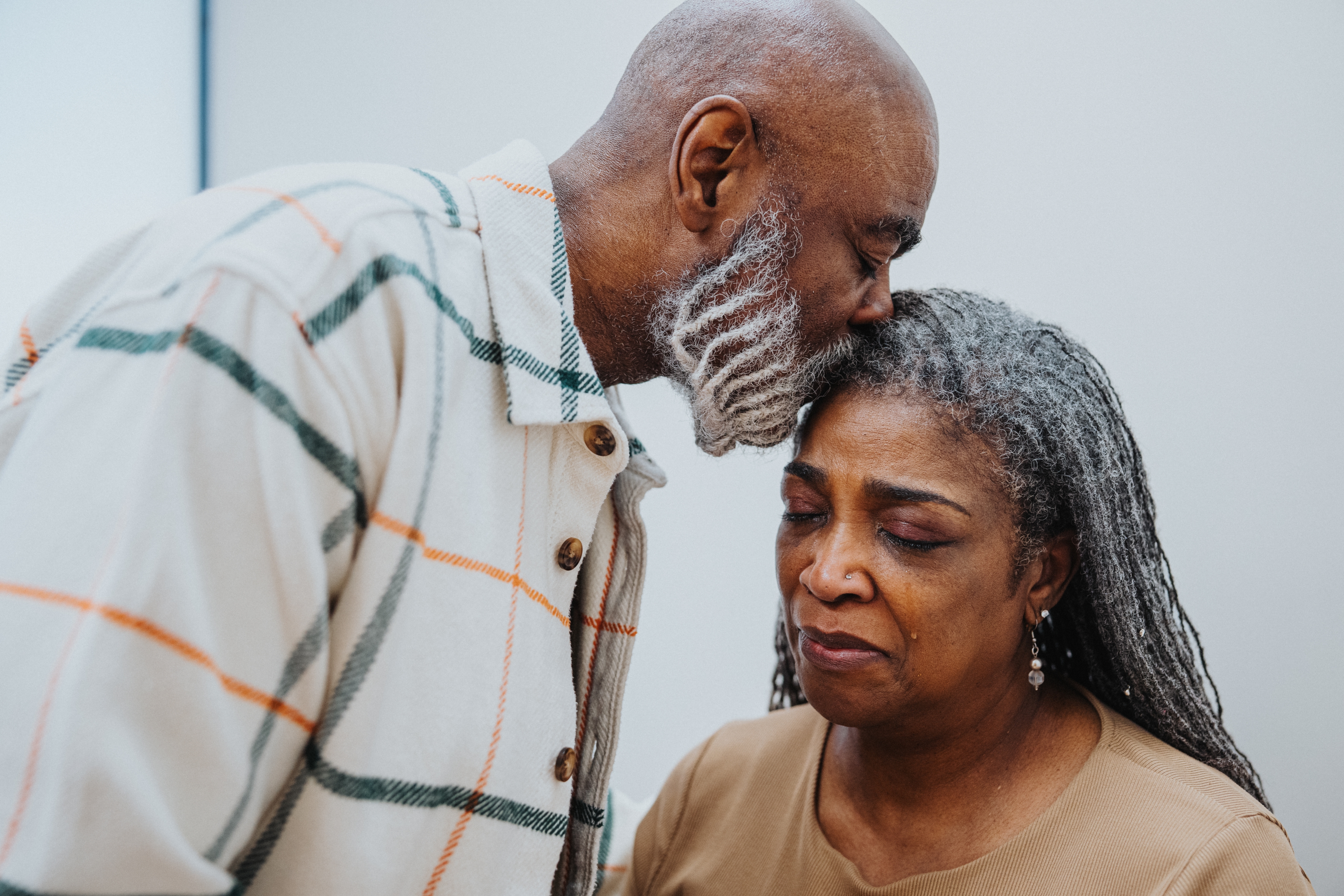 Elderly man gently kisses a woman's forehead; both display a tender, emotional moment
