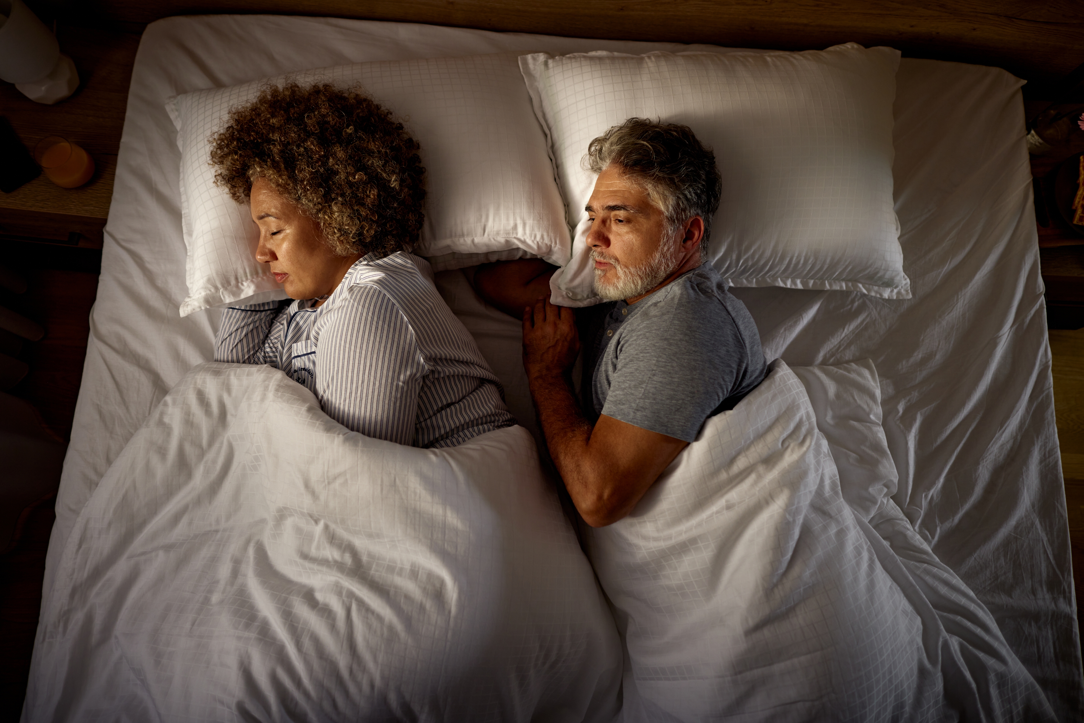 A couple lies back-to-back in bed, seemingly upset or in disagreement, each looking away from the other
