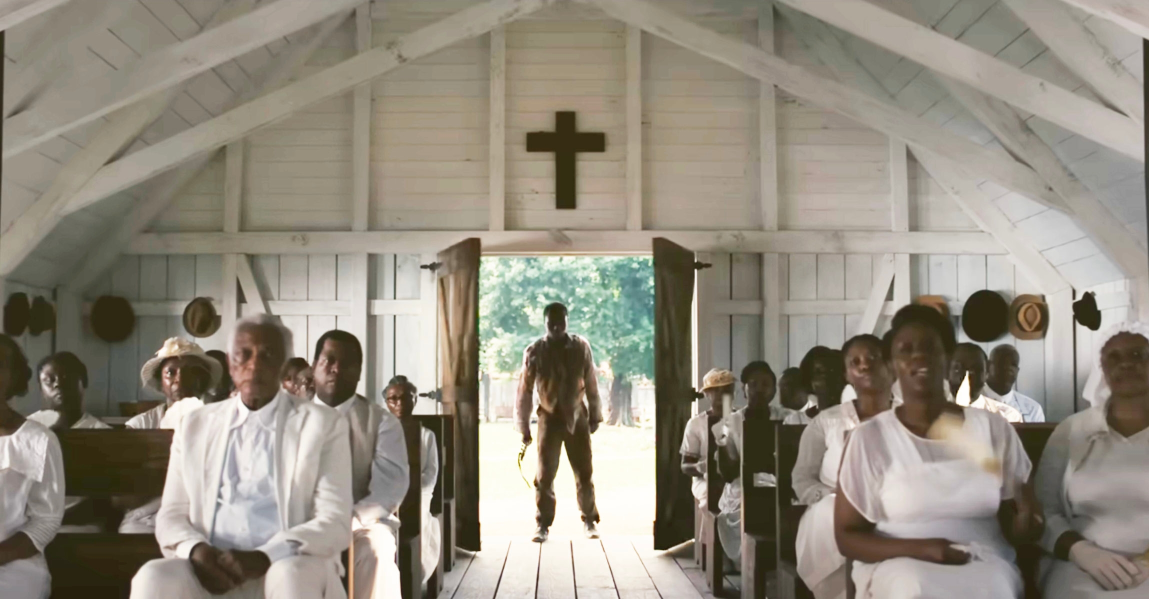 Sammie standing in the doorway of the church, as churchgoers sing and a cross hangs on the wall