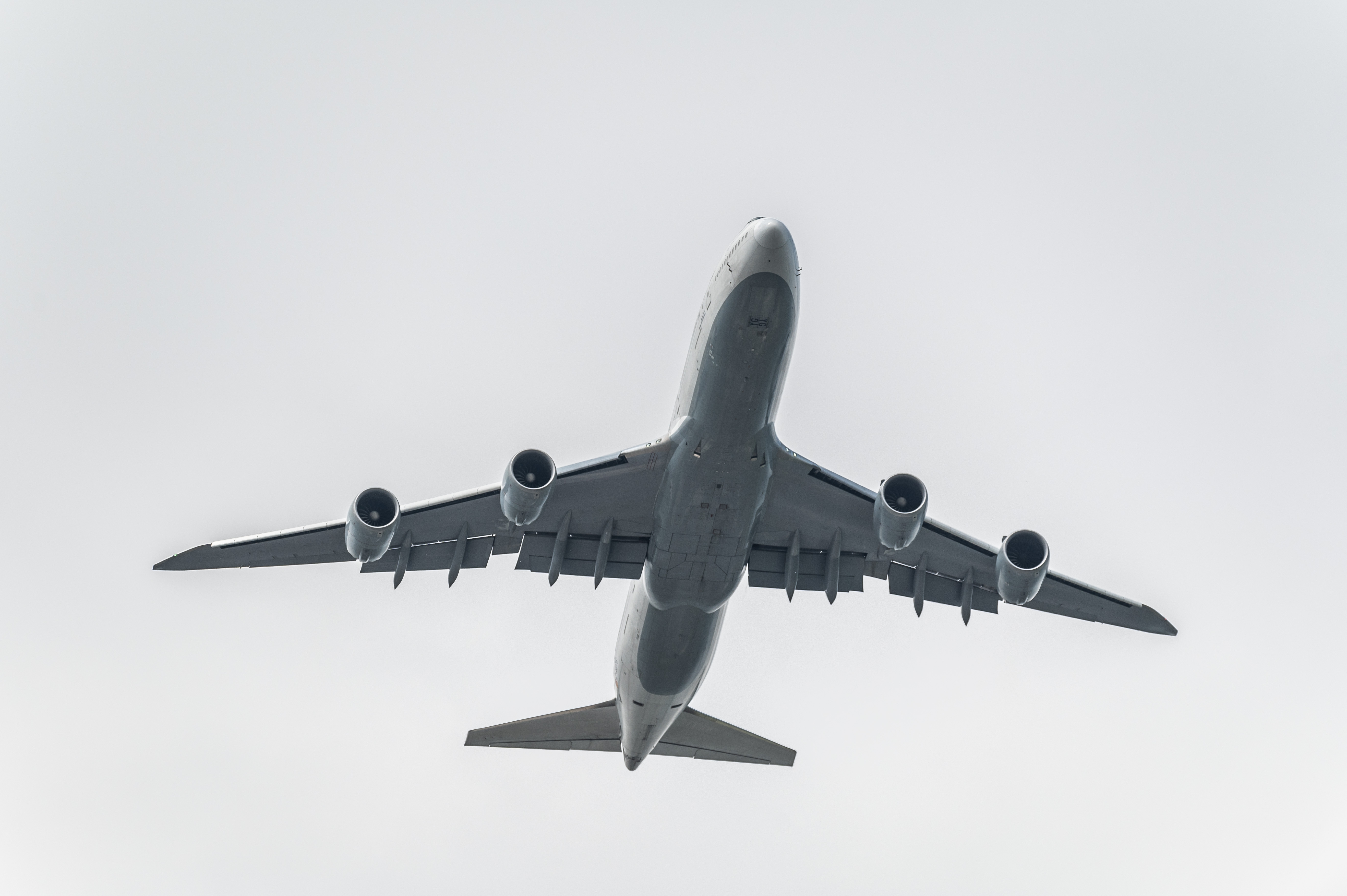 Airplane flying overhead against a cloudy sky, showing its underbelly and four engines