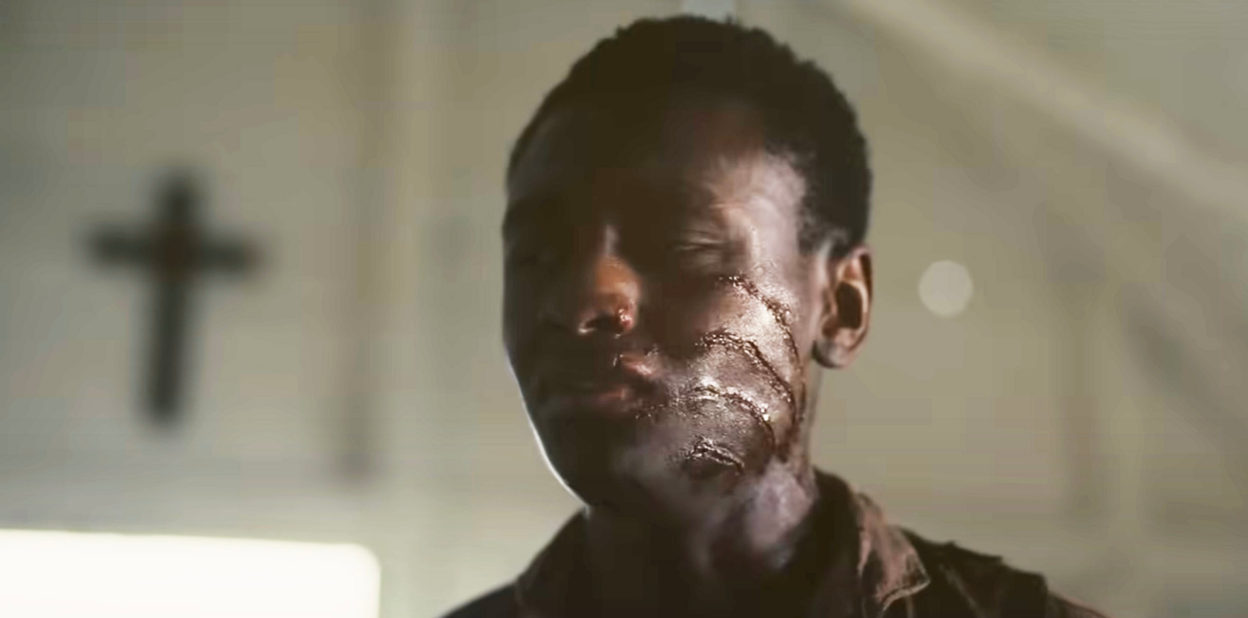 Sammie standing in the church with slashes on his face and a cross in the background