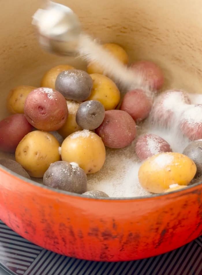 Boiling mixed babe potatoes successful an orangish pot, stirred with a spoon, showing cooking progress
