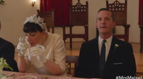 A woman in a white dress with a floral headpiece is seated at a table with a man in a suit at a wedding