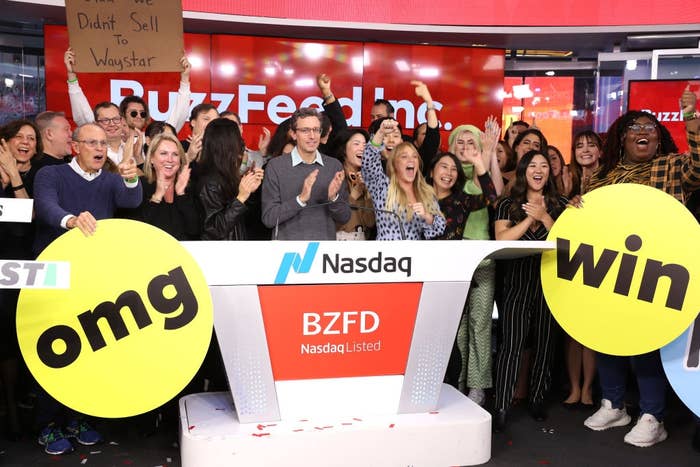 People observe astatine a Nasdaq lawsuit with a "BuzzFeed Inc" banner and yellowish signs saying "omg" and "win." A idiosyncratic holds a motion speechmaking "We Didn’t Sell To Waystar."