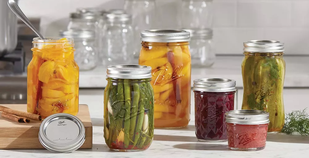 Mason jars filled with preserved foods on a kitchen counter with text: &quot;#1 Most Trusted Mason Jar Brand. Preserve with Confidence - Lock In the Perfect Seal.&quot;