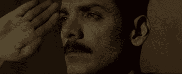 Person with a mustache tears up while saluting solemnly, conveying deep emotion and respect