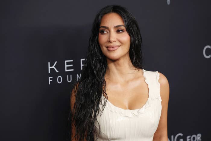 Kim Kardashian on a red carpet wearing a sleeveless, fitted dress with ruffled neckline, smiling and posing for photos