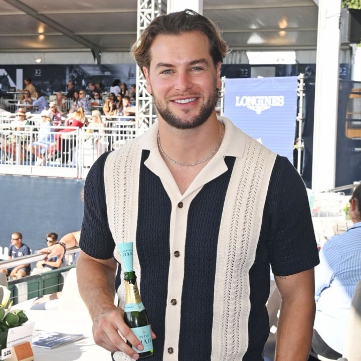 Person in a casual knit shirt and light pants holding a drink, smiling at an outdoor event