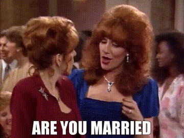 Two women speaking animatedly at a social event. One asks, "Are you married?"