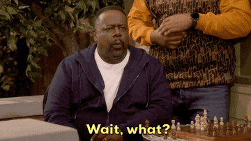 A man in a living room setting reacts with surprise, saying, "Wait, what?" while sitting at a table with a chessboard