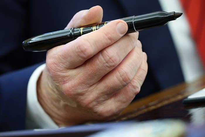 A hand holds a large black marker pen above a desk, suggesting upcoming writing or signing