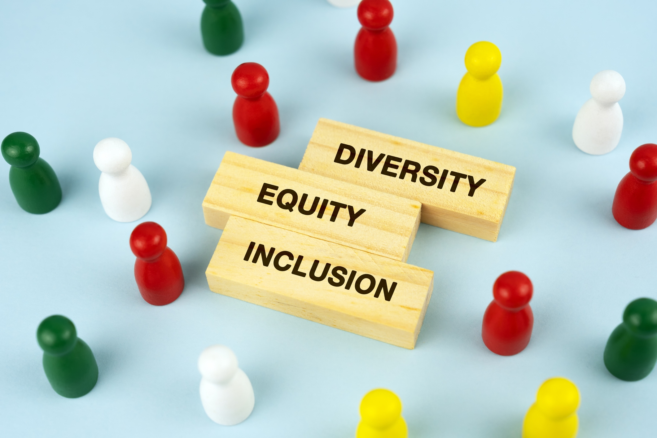 Wooden blocks read "Diversity," "Equity," and "Inclusion," surrounded by multicolored game pieces
