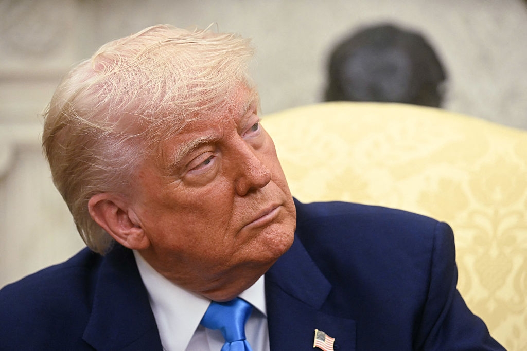 A person in a suit and tie is seated, looking to the side with a serious expression