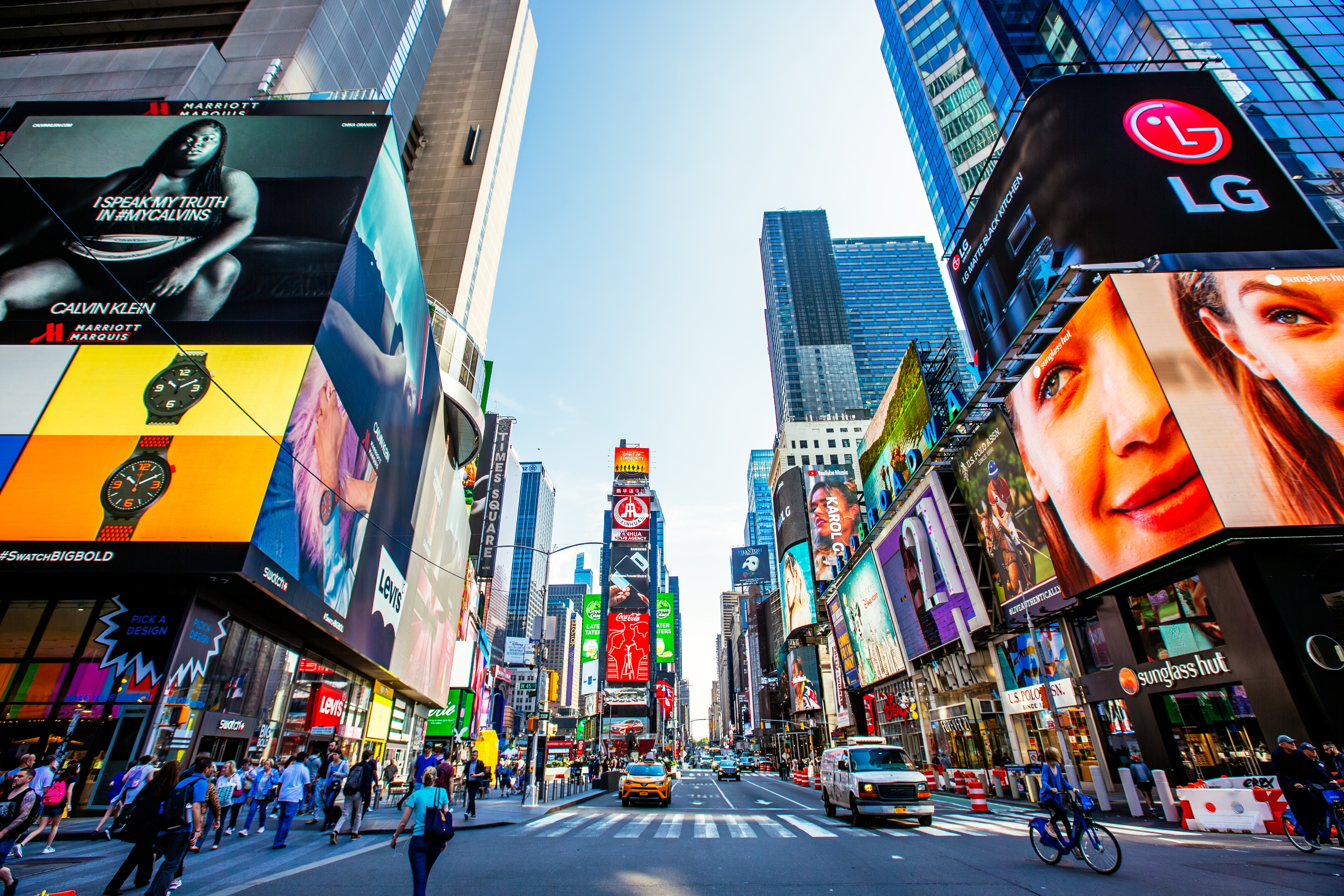 Bustling Times Square with numerous large digital billboards, taxis, and crowds, showcasing a lively urban scene