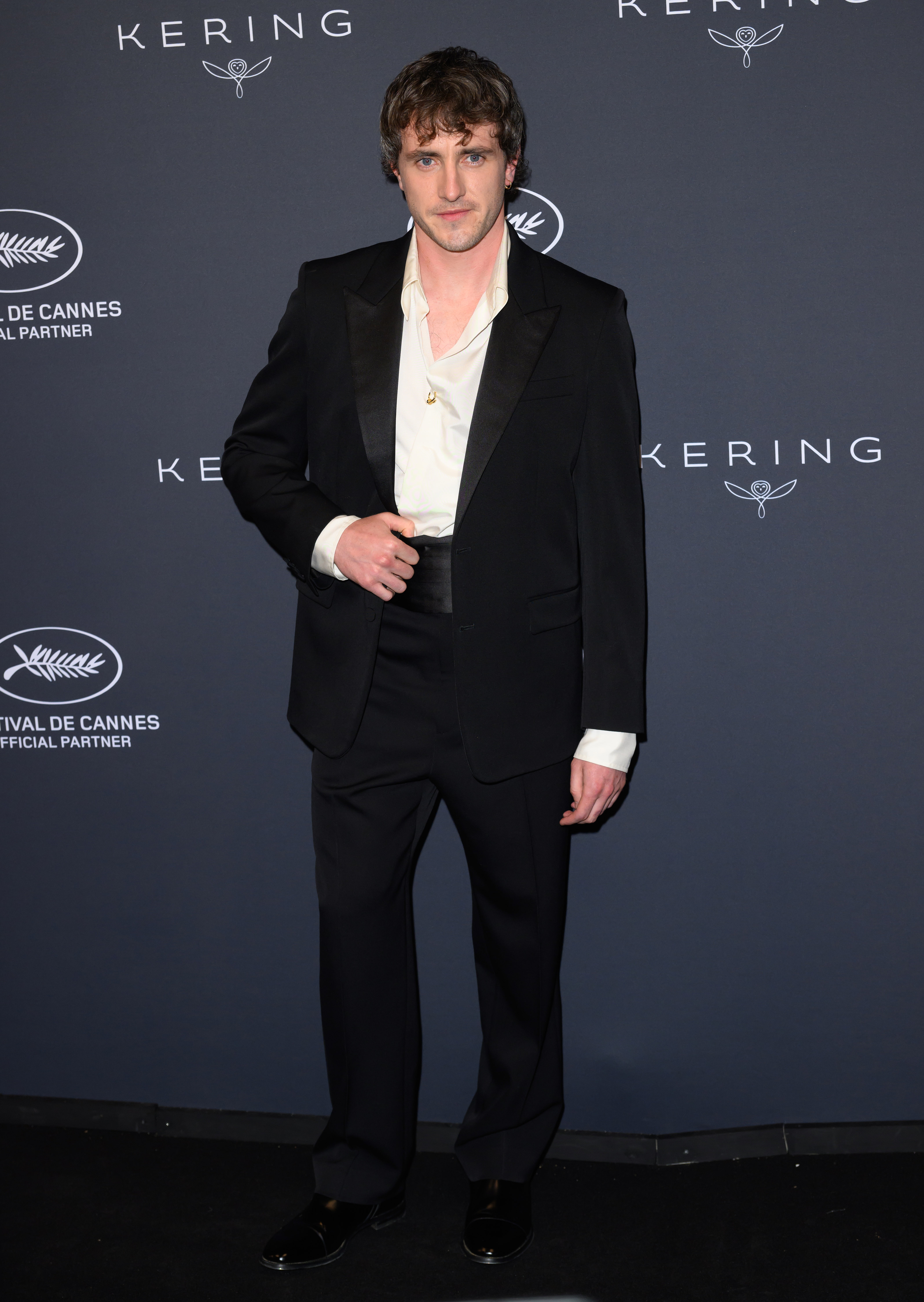 Paul Mescal on the red carpet in a classic tuxedo with an open-collared shirt, posing confidently