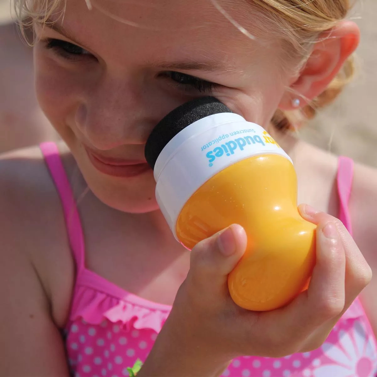 Child using a sunscreen applicator on her face, smiling, wearing a swimsuit