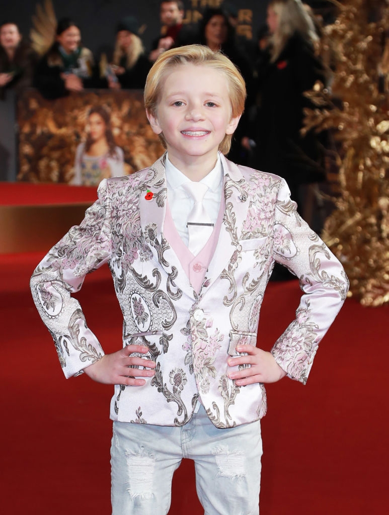 Child Dexter on red carpet in a floral, brocade-style suit, smiling with hands on hips