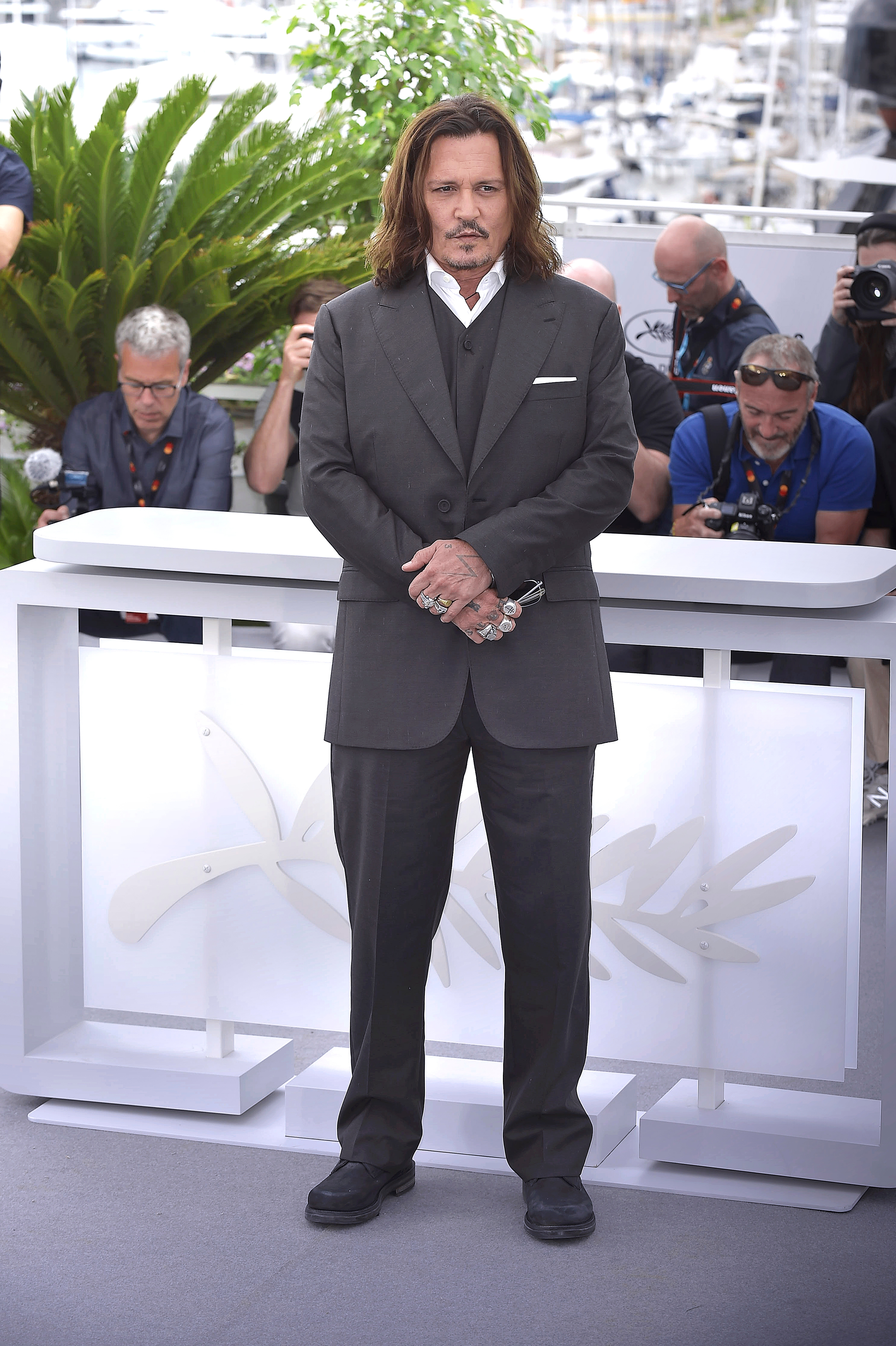 Actor in a tailored suit stands at a press event with photographers in the background