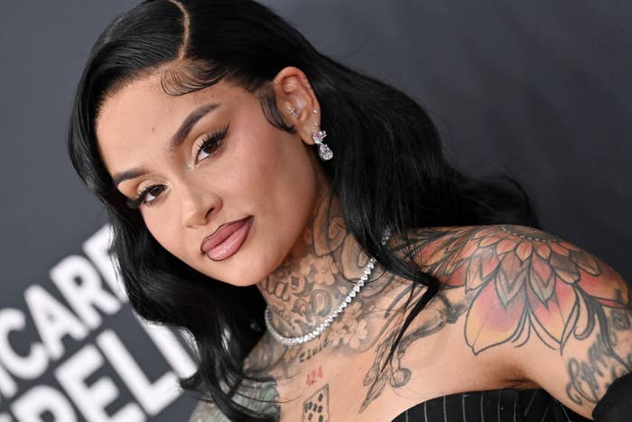 Kehlani with long hair and tattoos in a striped top at an event, posing confidently