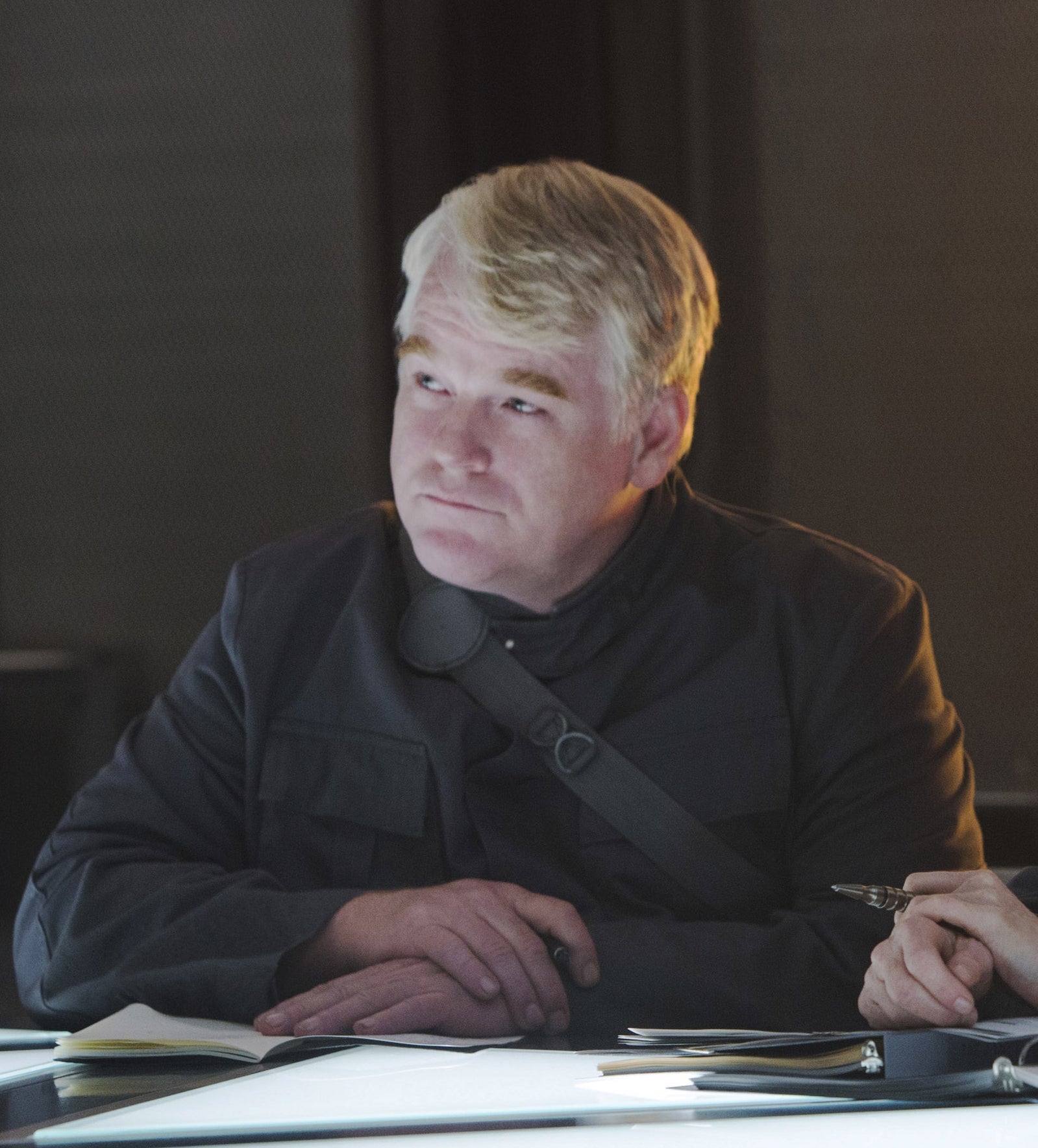 Phillip in a dark shirt, seated at a table with arms folded