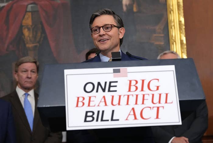 A person standing at a podium, speaking, with a sign reading "One Big Beautiful Bill Act." Other individuals are in the background