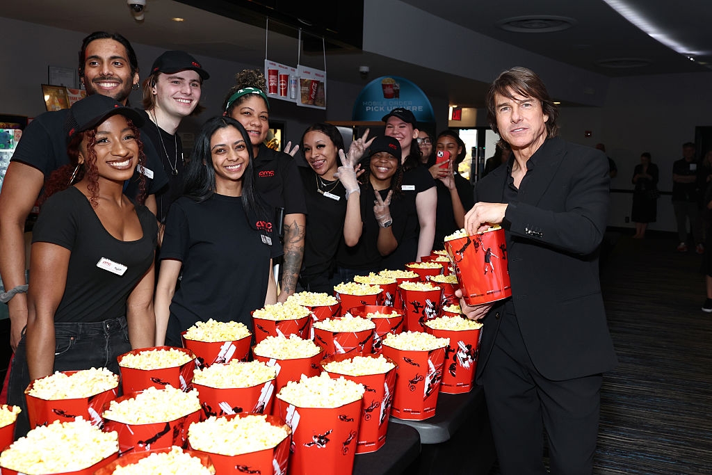 A well-dressed man poses with a group of cinema staff, standing beside a table filled with popcorn buckets