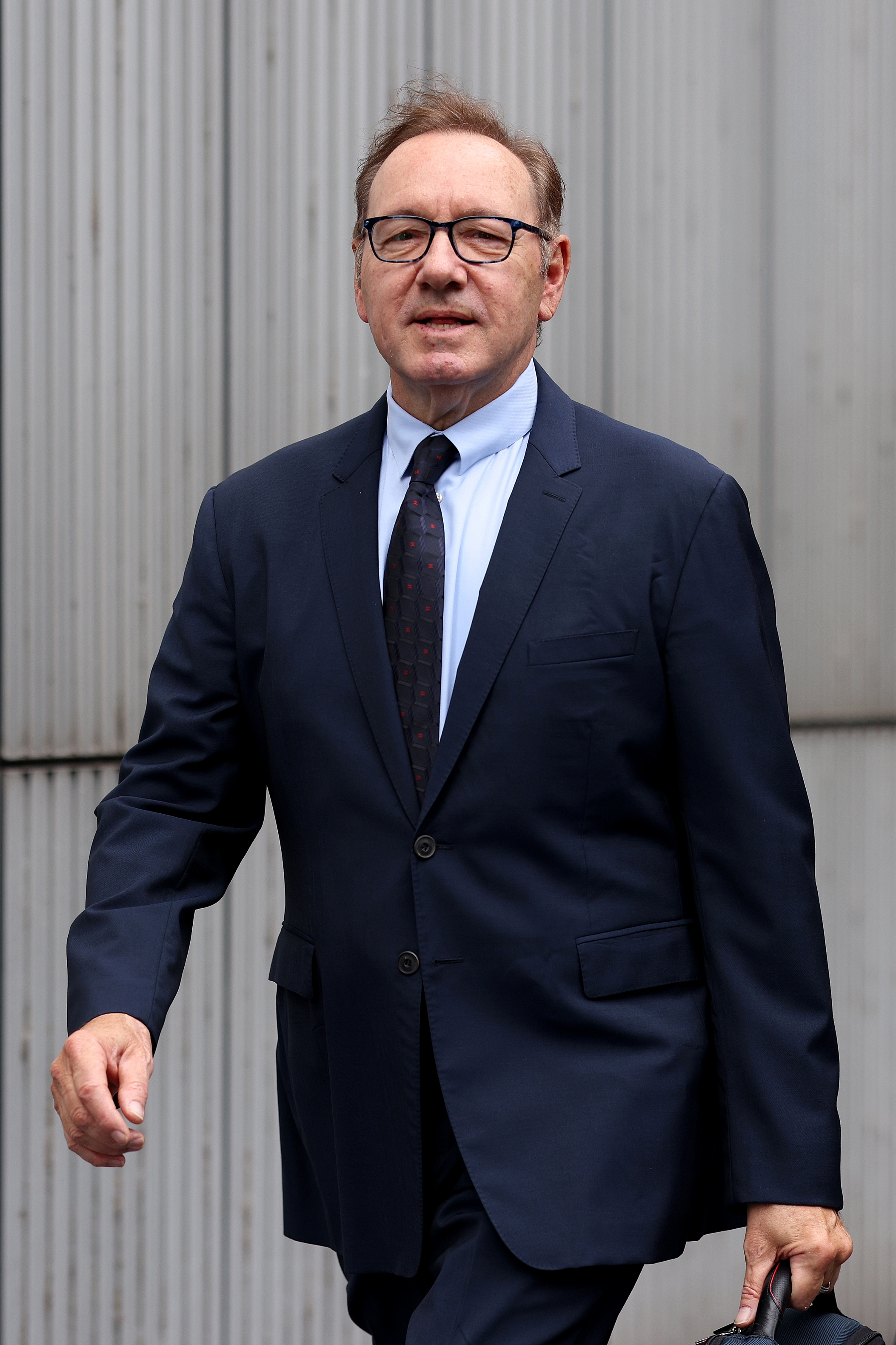 Person in a formal suit with a patterned tie, walking outdoors