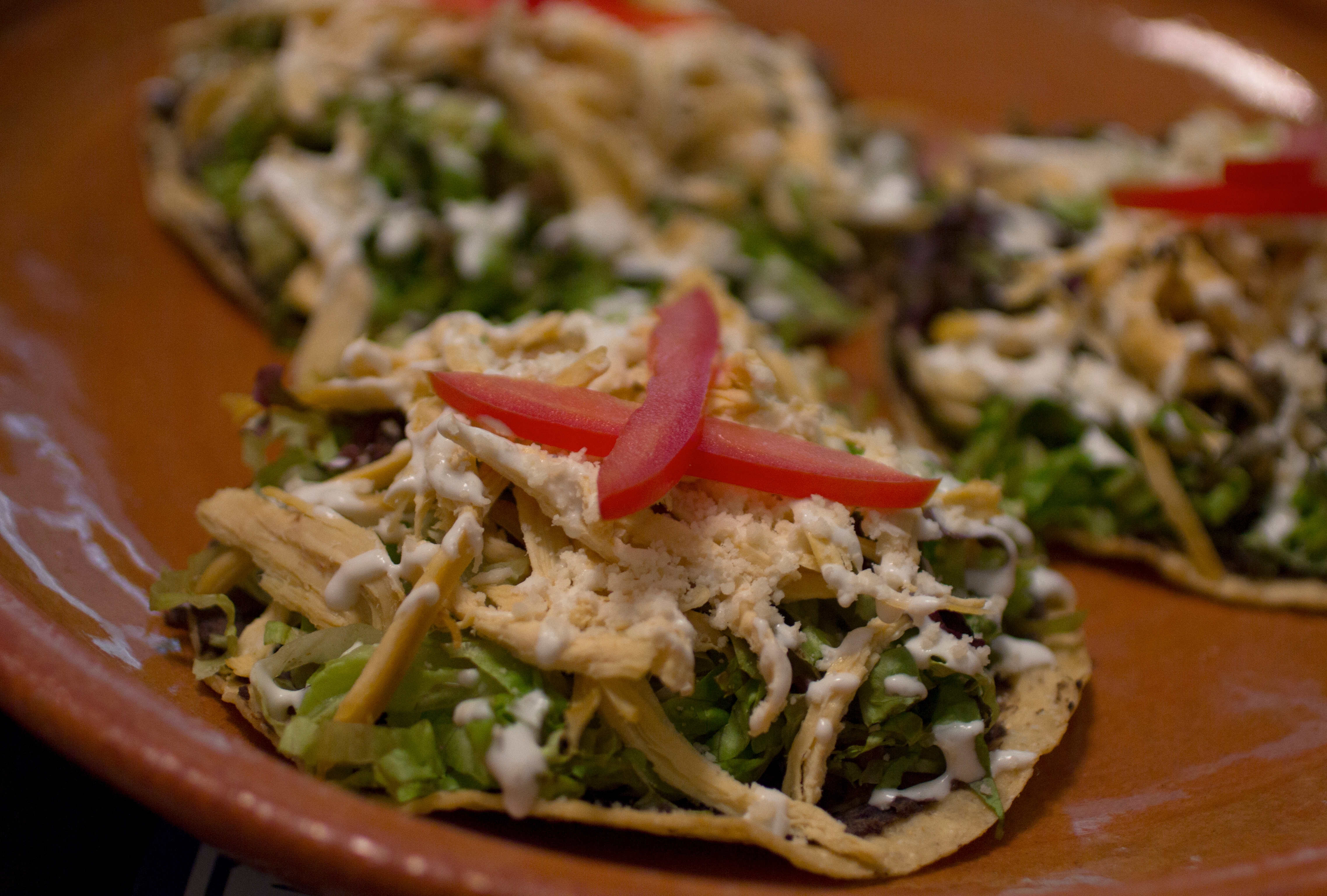 Plate of loaded tostadas topped with shredded chicken, lettuce, cheese, and sliced tomatoes