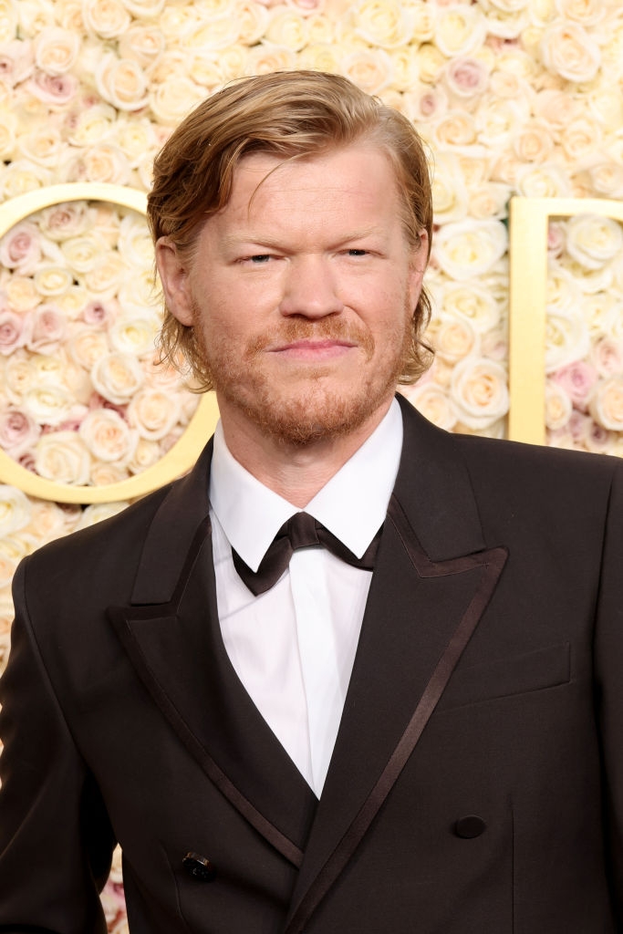 Jesse in a dark, stylish suit stands in front of a floral backdrop