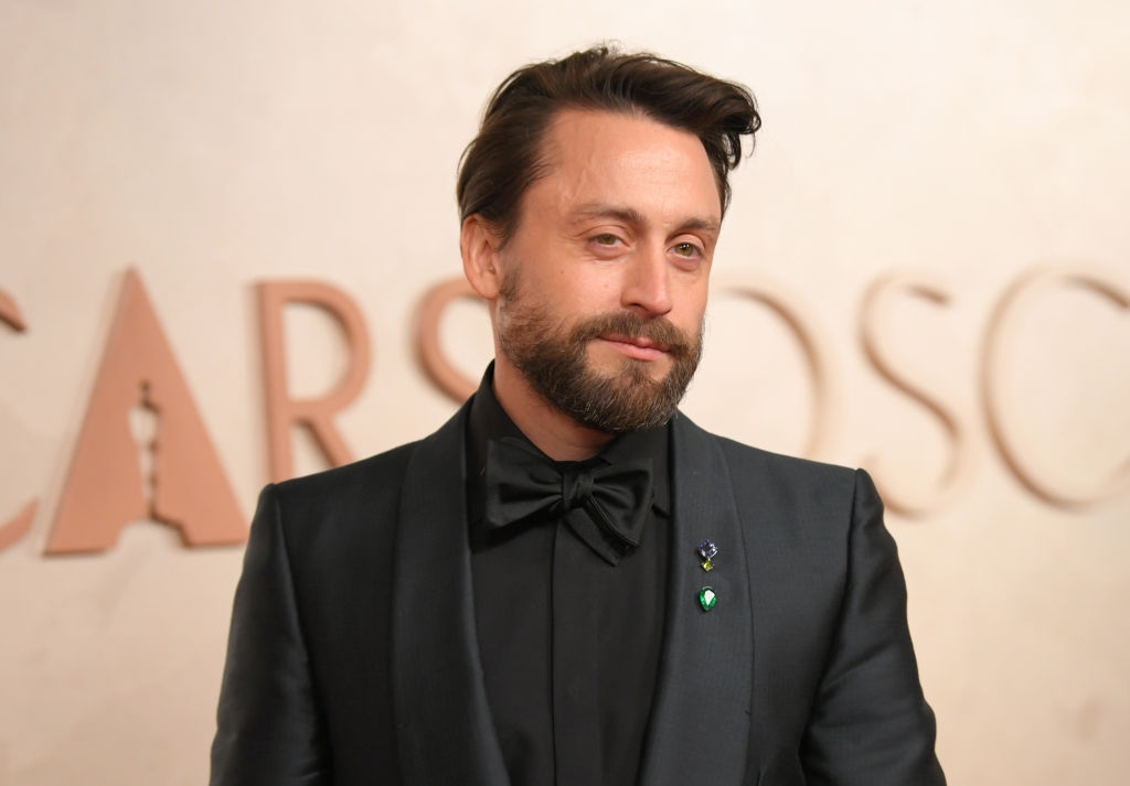 Kieran in a sleek suit with a bow tie, standing on a red carpet at a formal event