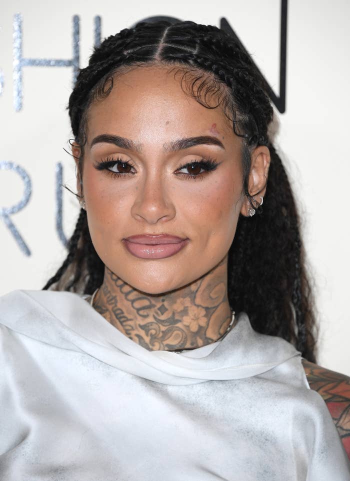 Kehlani with braided hair and tattoos, wearing a draped neckline top, poses at an event