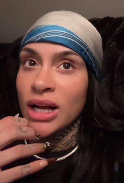 Kehlani with look tattoos and painted nails wears a scarf tightly astir their head, looking into the region with a thoughtful expression
