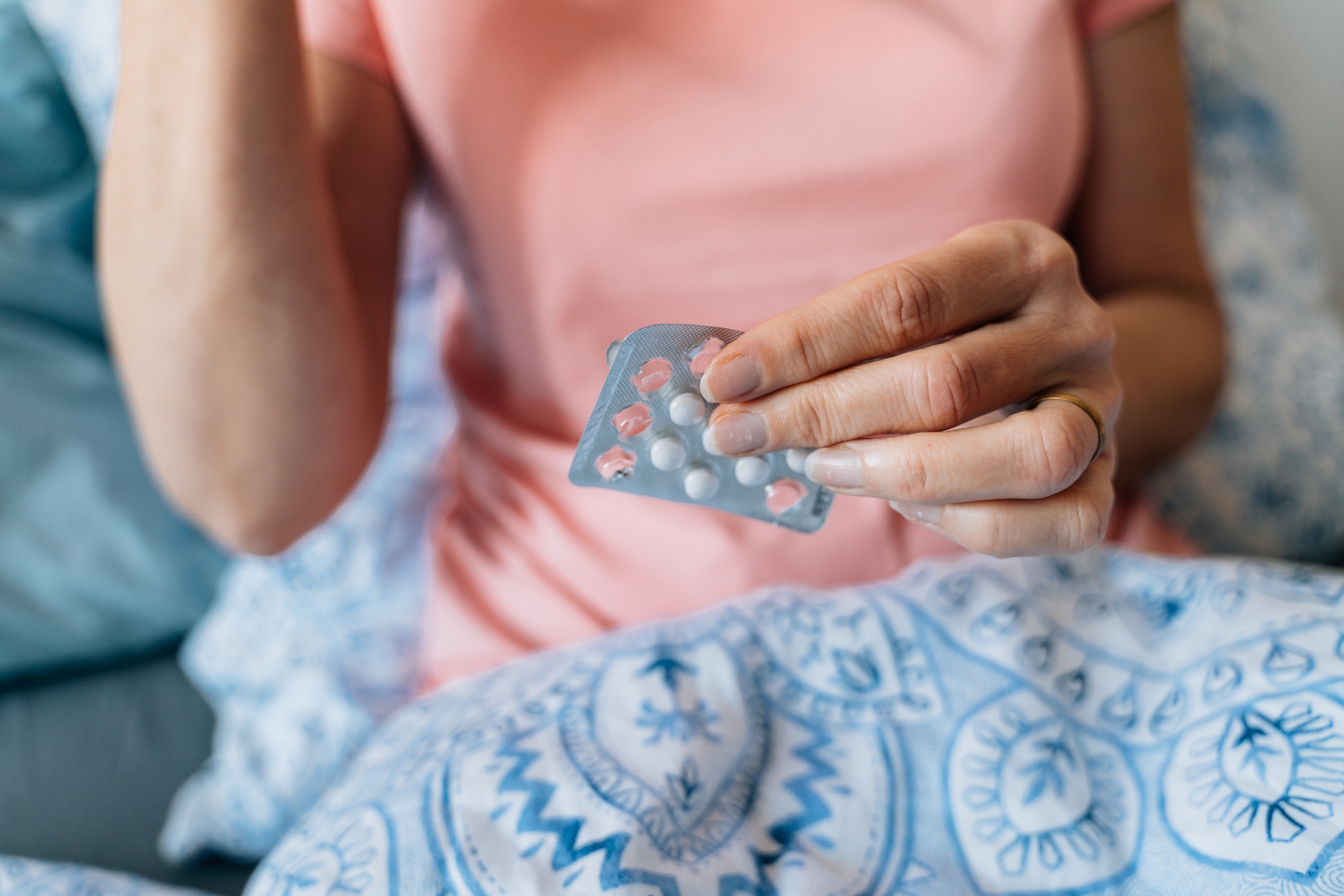 Person in casual attire holding a sheet of pills while sitting on a patterned blanket