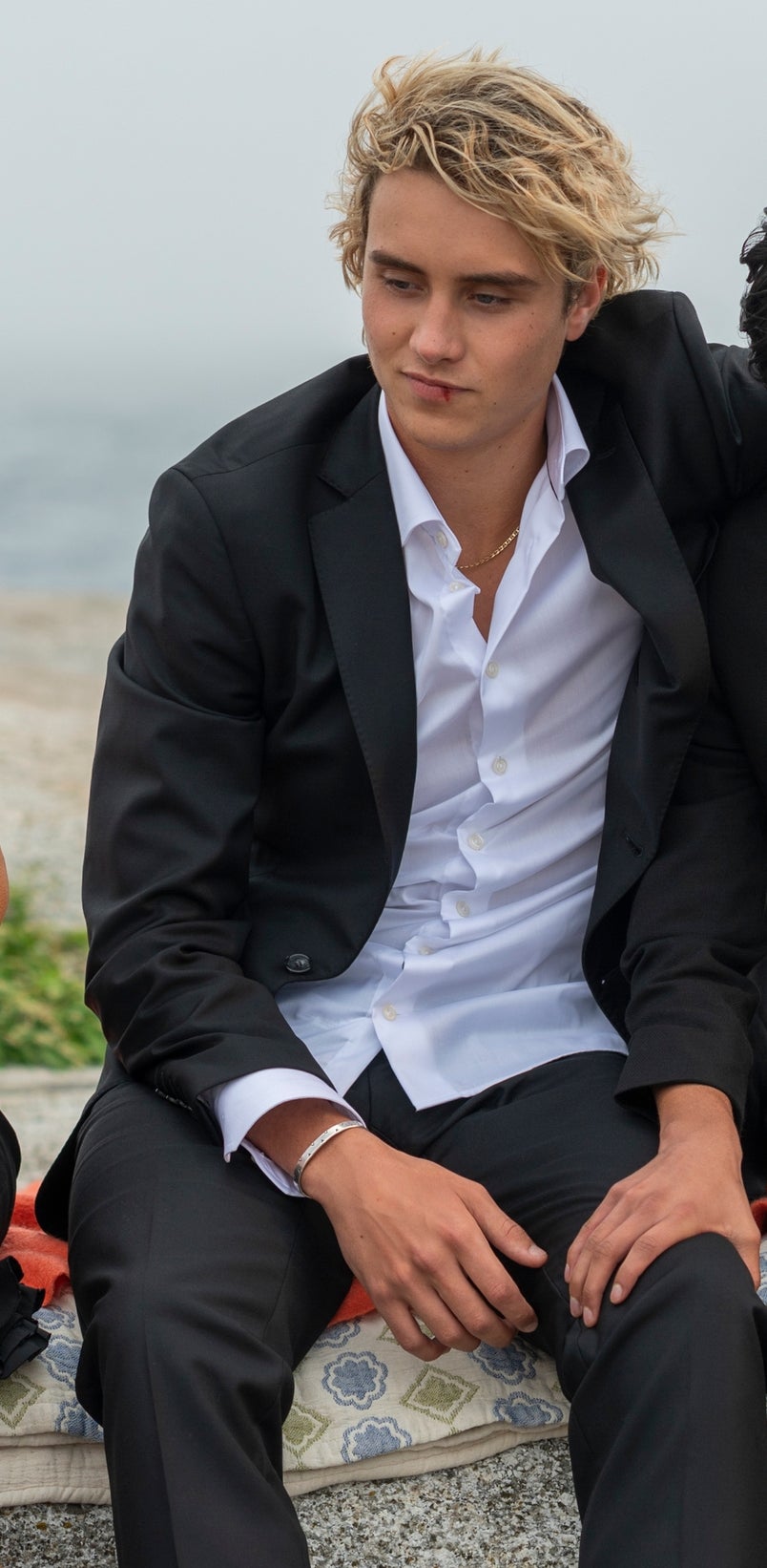 Jospeh in a suit, sitting on a rock wall by the sea