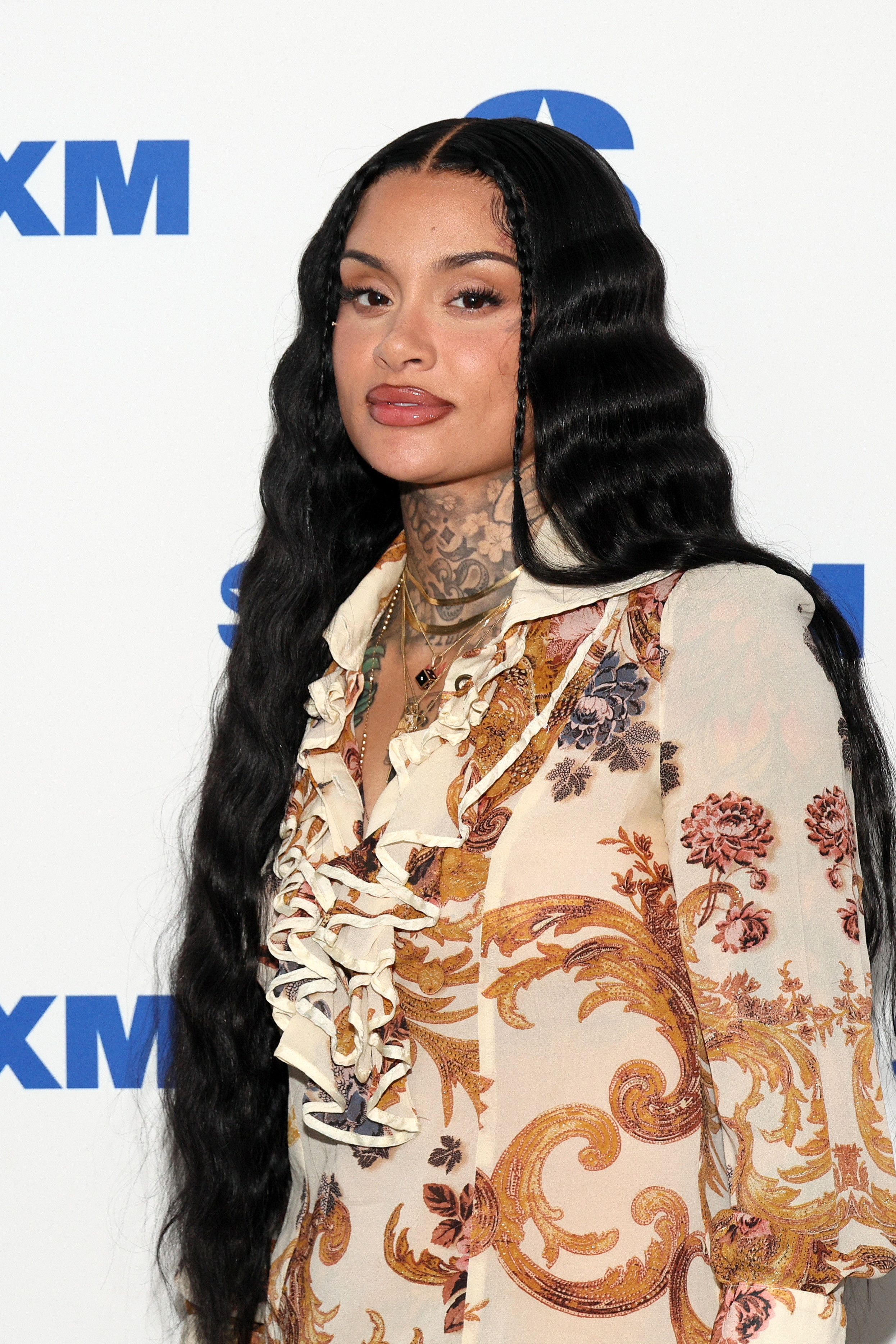Kehlani with long hair and a floral patterned blouse with ruffles poses for a photo at a media event