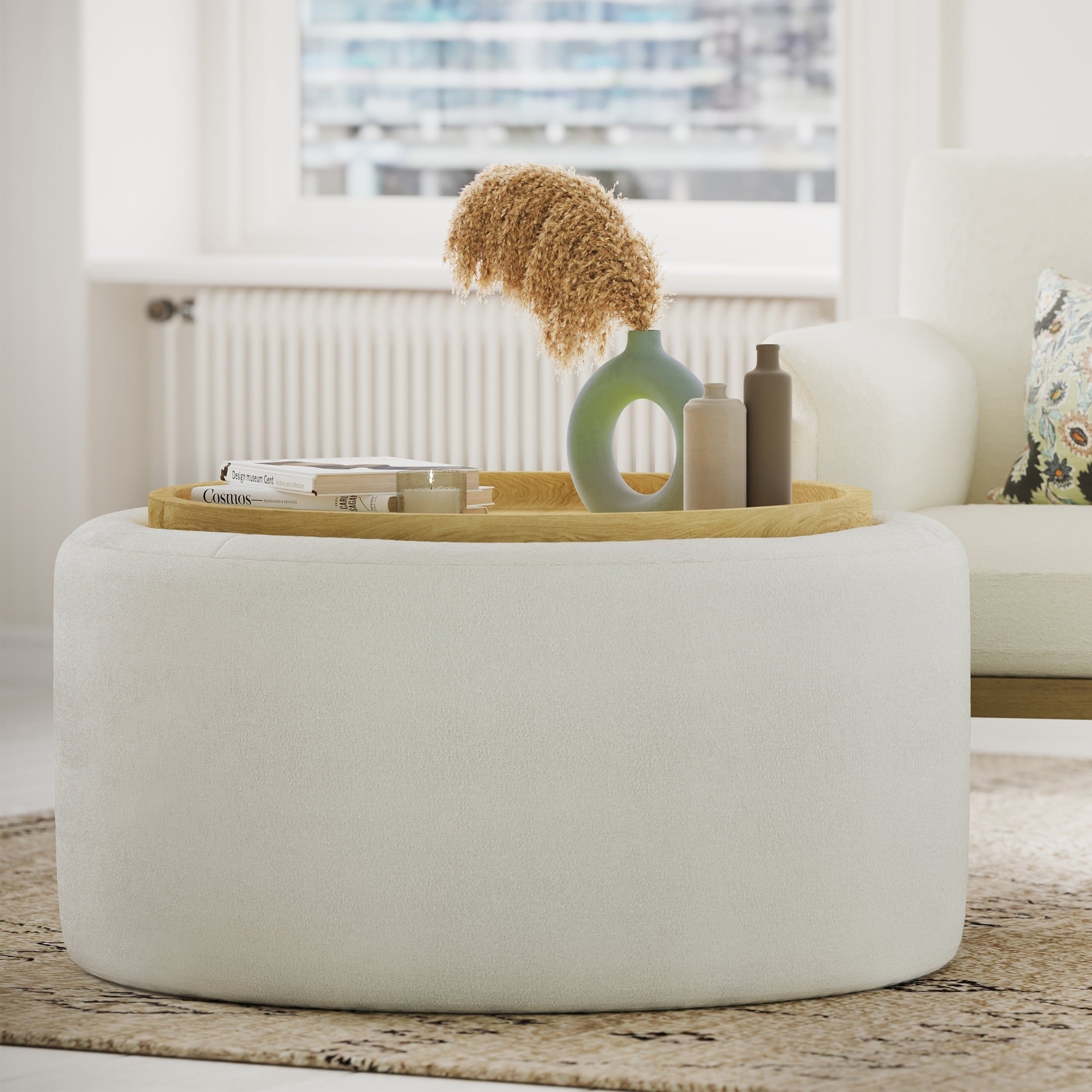 Round achromatic  ottoman holds a tray with a vase of dried flowers, 2  bottles, and a book, placed successful  a modern   surviving  room