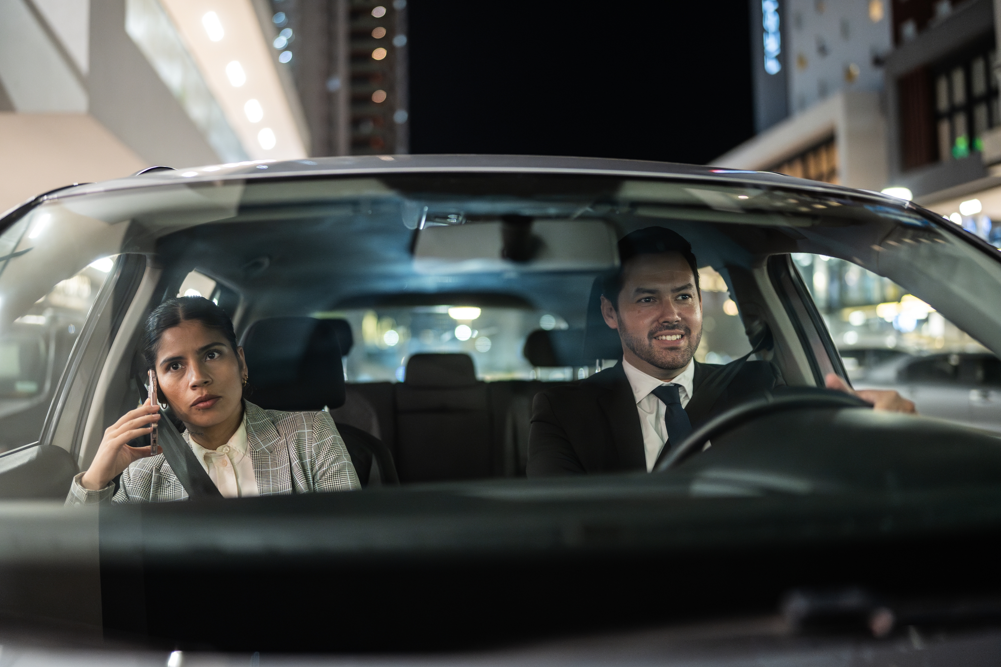 A couple in a car at night; the woman talks on the phone while the man is smiling and driving