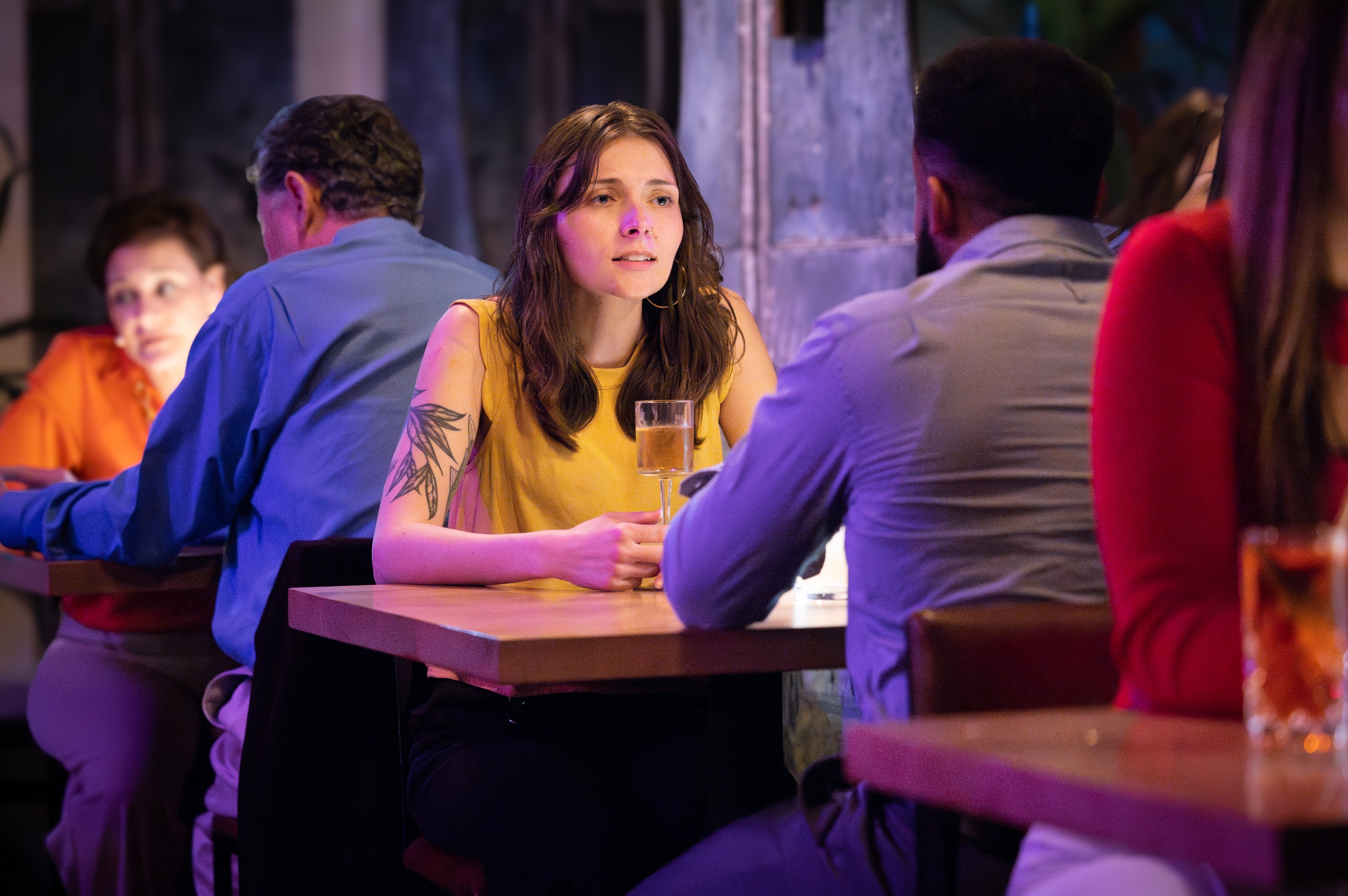 Two people sit across from each other at a table in a lively bar, engaged in conversation