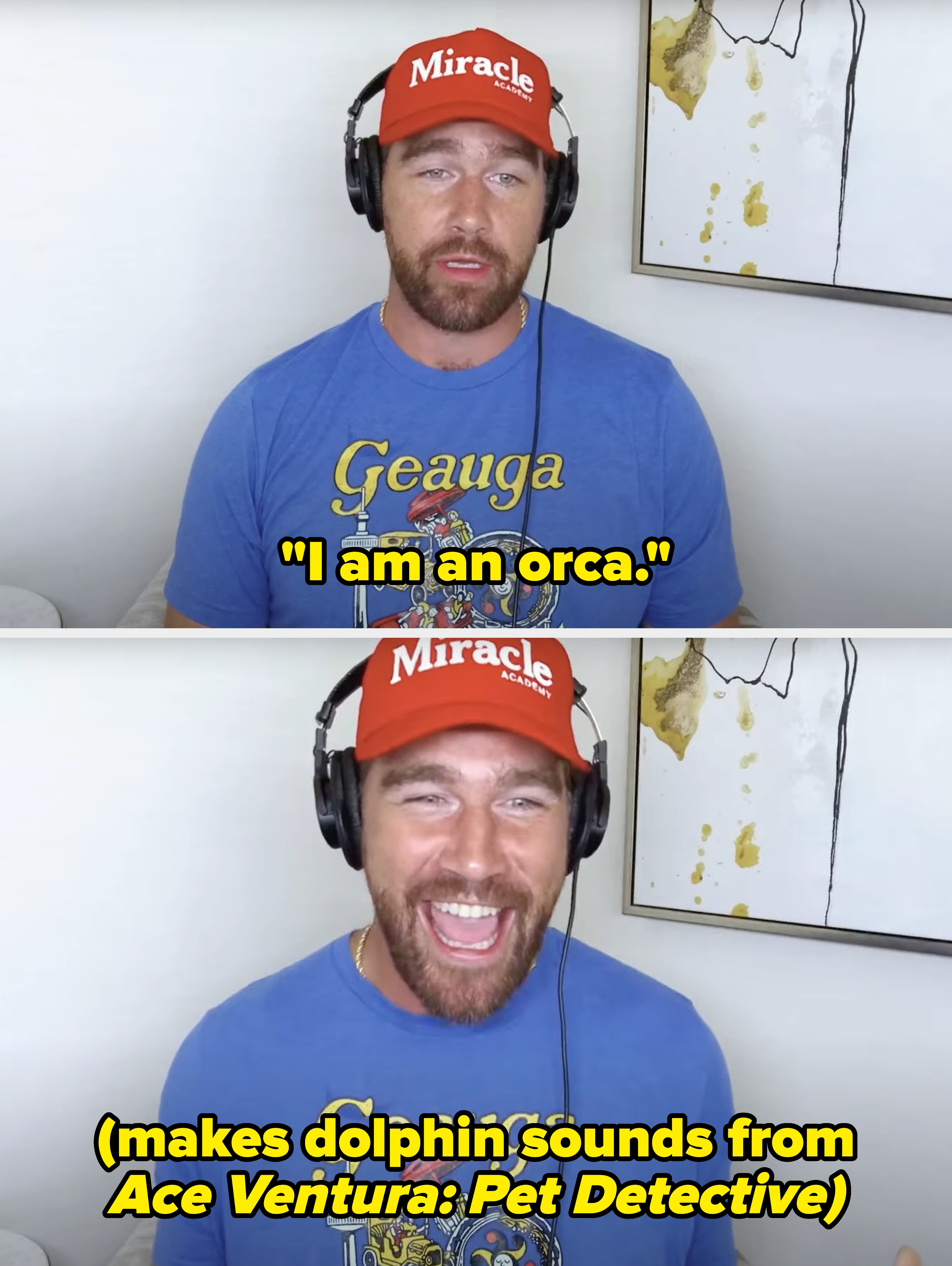 Man wearing headphones, red cap, and blue t-shirt with cartoon design, sitting indoors in front of a white wall with a painting