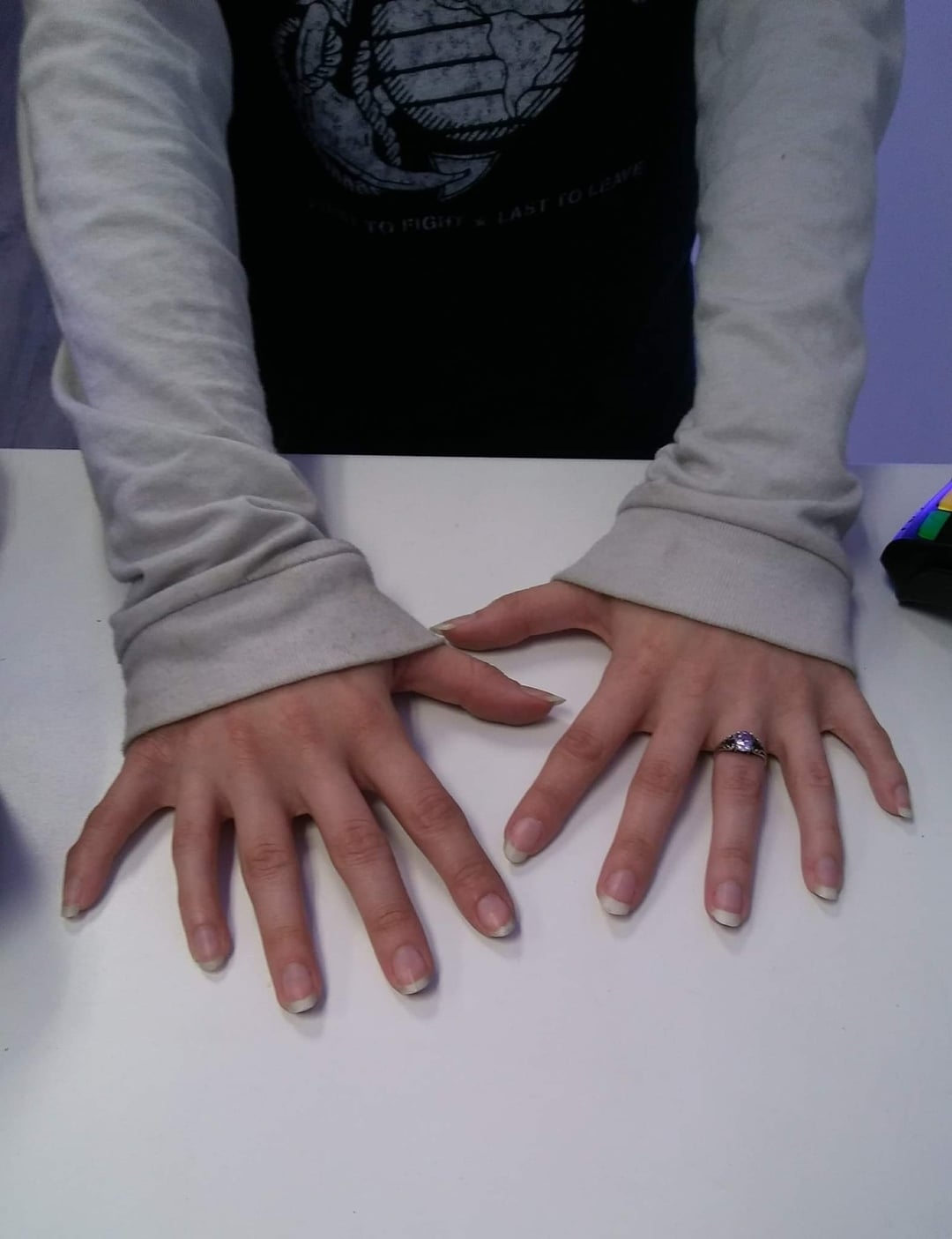 Person with long-sleeved shirt showing their hands on a white surface; one hand wears a ring