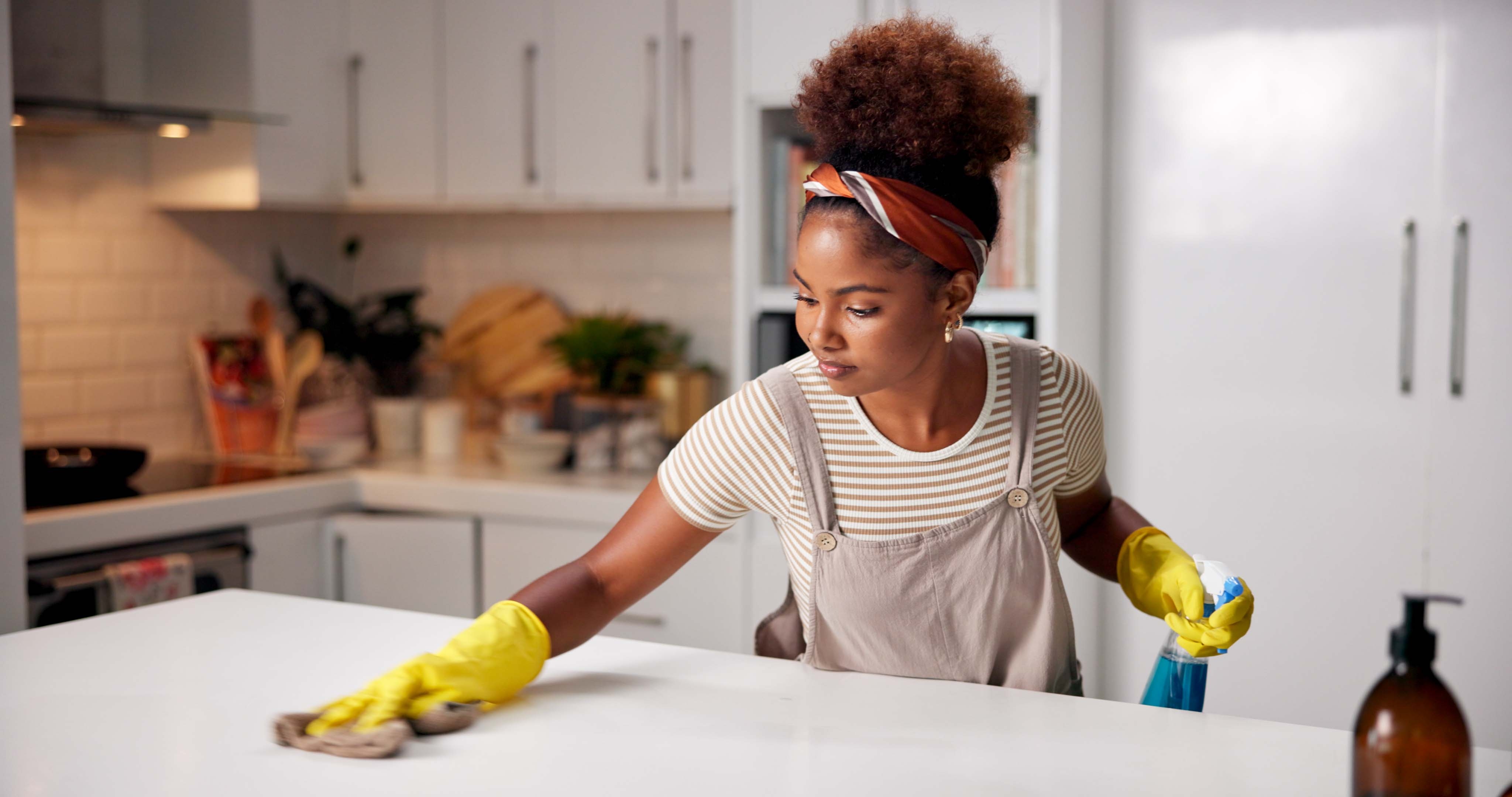 Person in casual attire cleaning a kitchen counter with gloves and a cloth, focusing intently on their task