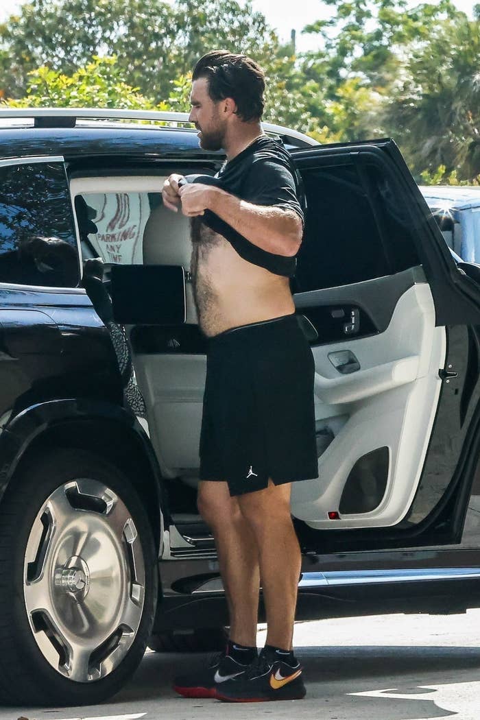 Man dressed in casual black athletic wear adjusts shirt at open car door