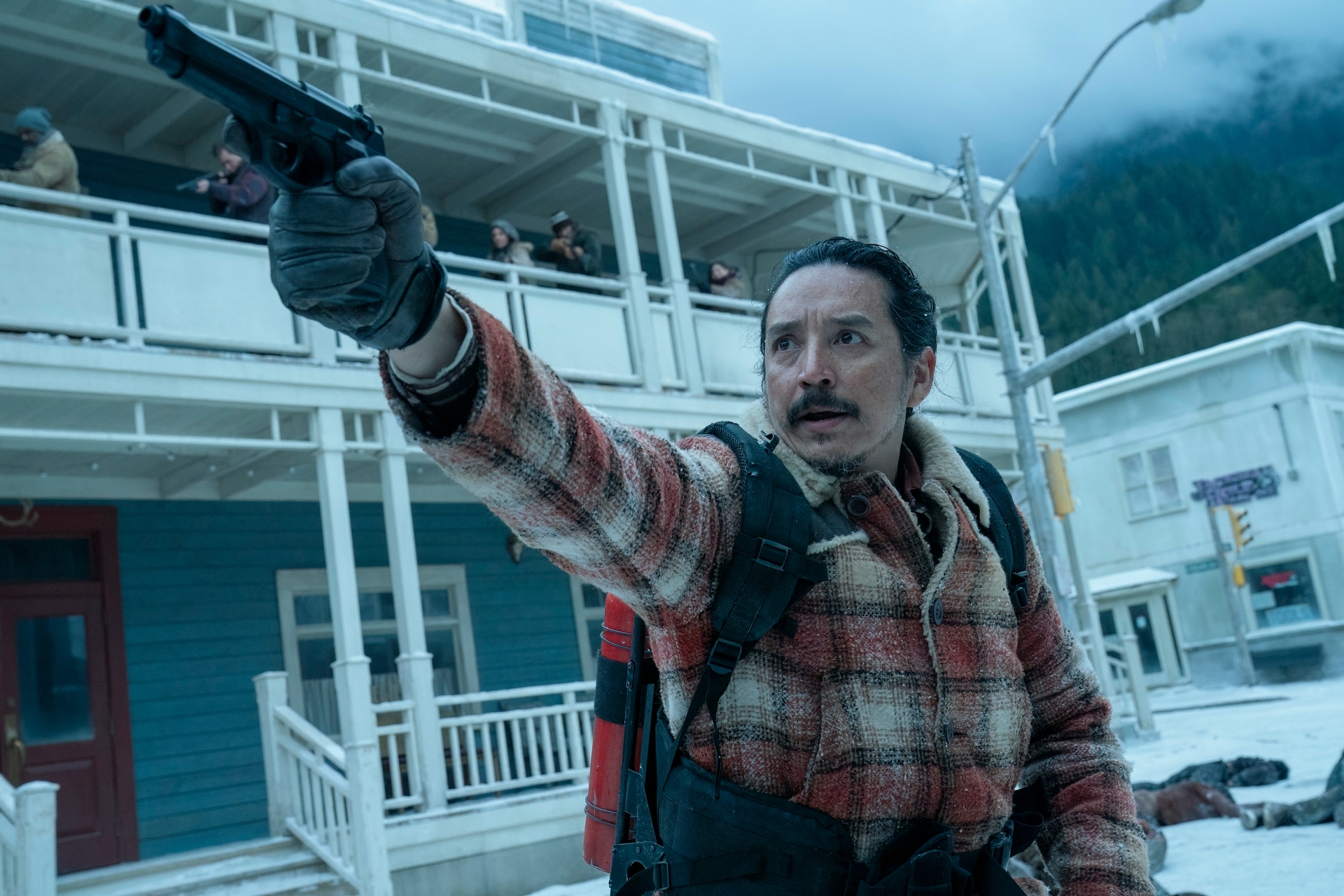 Tommy in a plaid jacket holds a gun in a snowy town setting