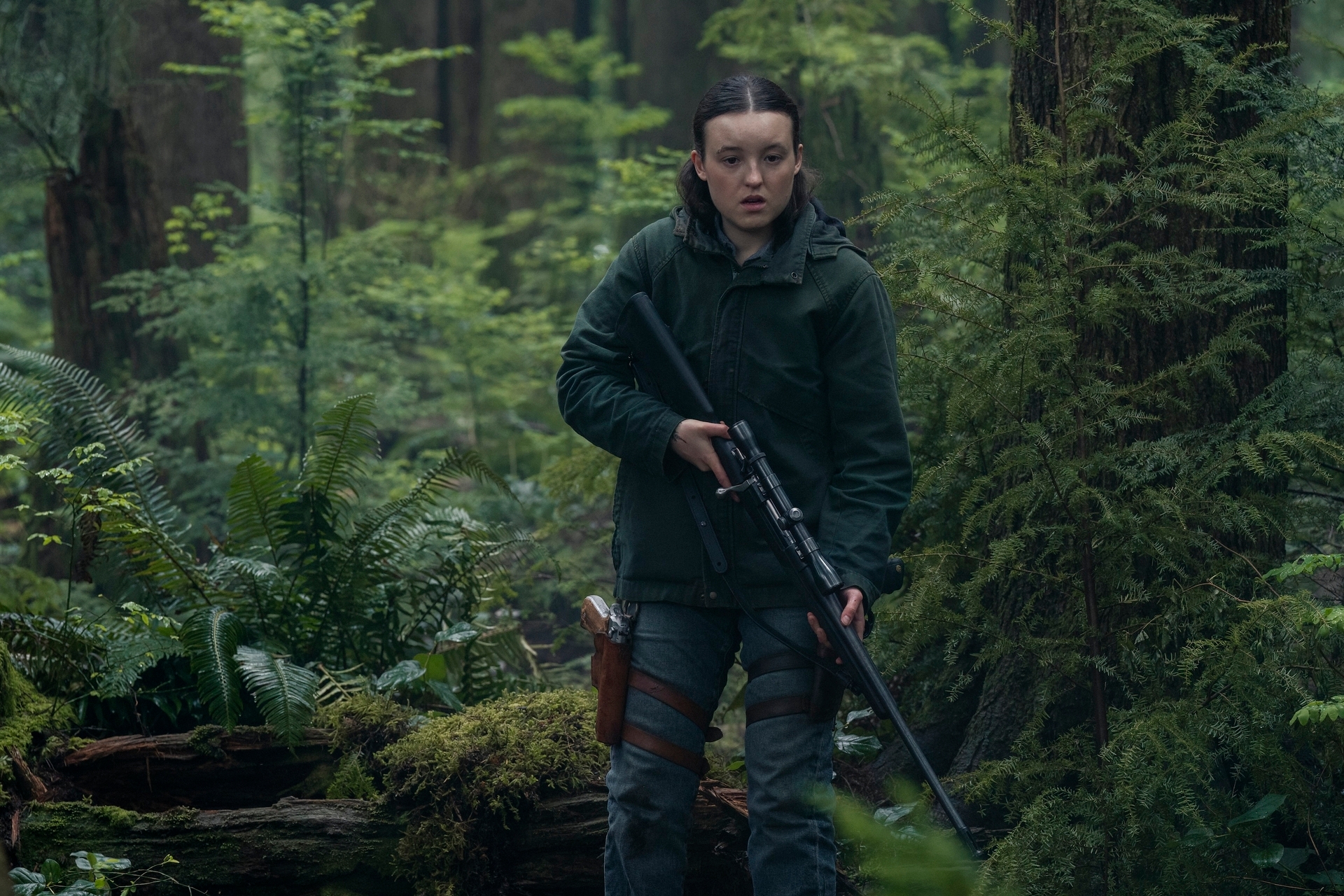 Ellie in outdoor gear holds a rifle, navigating a dense forest