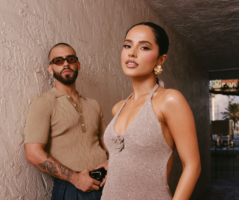 Dos personas posan; una lleva un vestido brillante con escote halter, la otra una camisa ajustada de punto. Ambiente elegante, relacionado con música