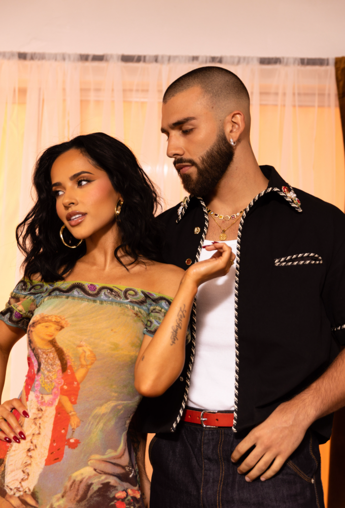 Dos personas posan. Una lleva un vestido con estampado artístico; el otro, camisa negra con detalles. Ambos tienen un estilo moderno