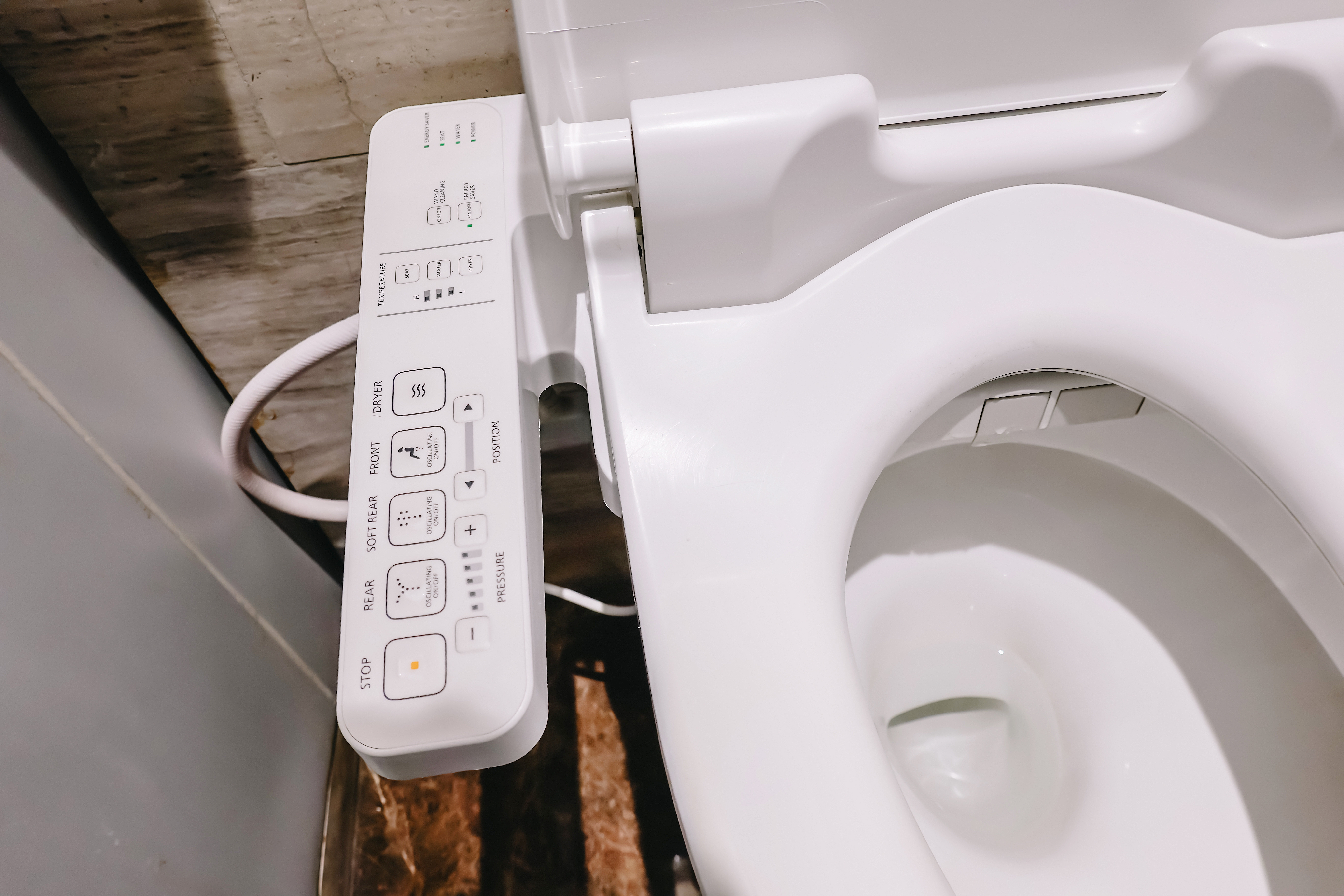 Bidet control panel with multiple buttons, including dials for water pressure, temperature, and different wash settings, next to a toilet seat